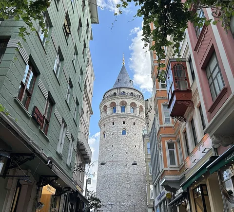 Daylight street approach to Galata Tower framed by neighbourhood shops and historic façades, 2024.