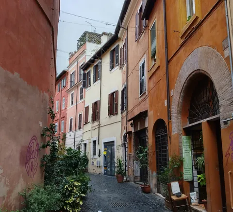 Quiet cobblestone Trastevere lane with ochre facades and plants.